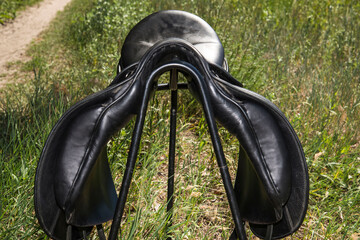 Black leather saddle for horse on a metal stand.