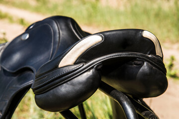 Back view of black leather saddle against blurred natural background.