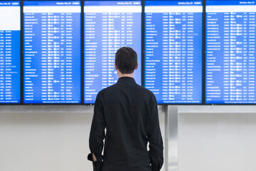Man standing at departure and arrival monitors at airport