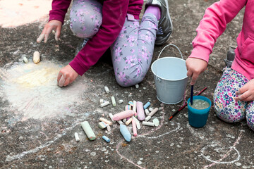 Children drawing with chalk on the concrete sitting on the ground. Art therapy, CBT, simple creativity excercises. Two girls drawing with colorful chalk. Outdoor activities, lifestyle