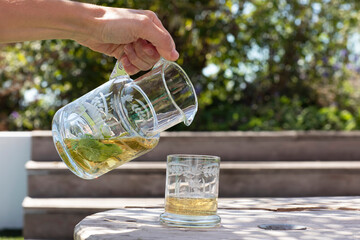 A female hand holding an etched glass carafe with healthy homemade juice and mint leaves next to a...