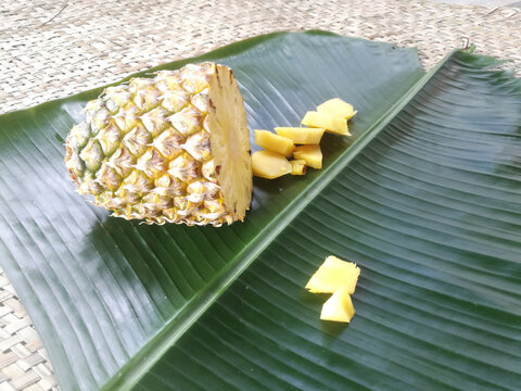 Pineapple and its slices placed in a green banana leaf.