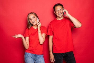 Obraz premium Attractive couple talking on their smartphones on red background