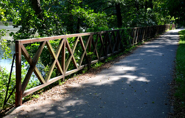 Obraz premium wooden fence made of beams painted brown and screwed into the shape of an x cross at the shore of a pond with a floating plank pier with a rope railing in a city park