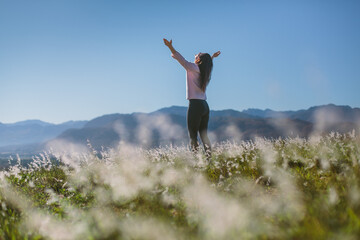 Beautiful woman standing in grass field with arms reaching for the sky in joy