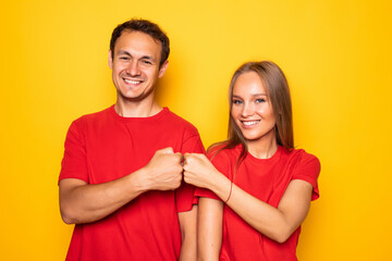 Cheerful young couple giving fists bump posing isolated on yellow background. People lifestyle concept.