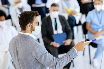 Fototapeta na wymiar Businessman wearing face mask while talking to large group of people on a seminar.
