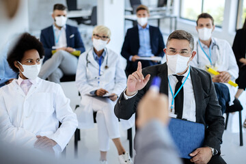Fototapeta na wymiar Businessman with protective face mask asking a question while attending a seminar.