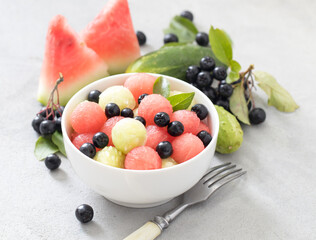 Salad of fresh watermelon balls, cucumber with black currant in a bowl on a light background