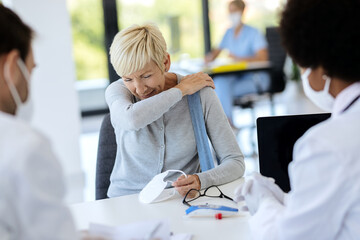 Mature woman sneezing into elbow while being at doctor's office.