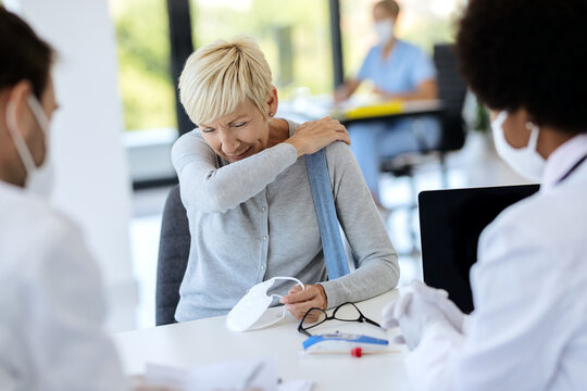 Mature Woman Sneezing Into Elbow While Being At Doctor's Office.