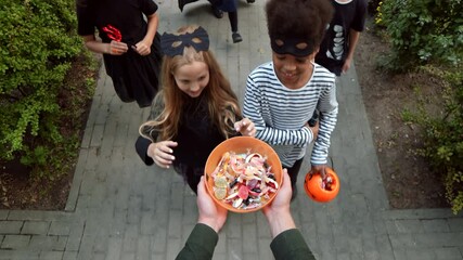 First person view of five diverse kids wearing cool Halloween costumes are talking different lollipops and candies out of bowl unrecognizable person holding in hands - Powered by Adobe