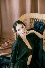 Obraz premium Young girl with dark hair in dark underwear and a silk peignoir on a wicker chair