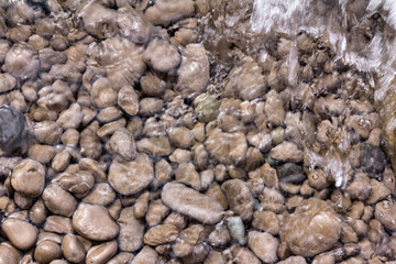 Sea stones in the sea water. Pebbles under water. The view from the top. Nautical background. Clean sea water. Transparent sea.