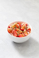 Vegetable salad of fresh tomatoes with onions and dill in a bowl on a light background