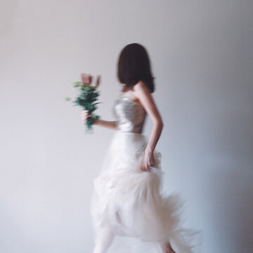 Woman wearing elegant evening gown moves swiftly, holding a bunch of flowers