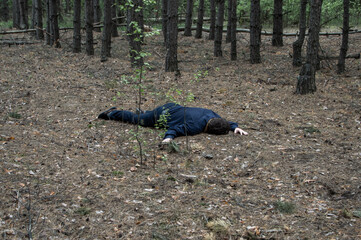 Murder in the woods. The body of a man in a blue shirt and trousers lies on the ground among the trees in the forest. Victim of an attack.