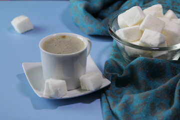Pile of white homemade marshmallows in a transparent bowl on a blue background. Cup of hot coffee and homemade marshmallows. Food concept.