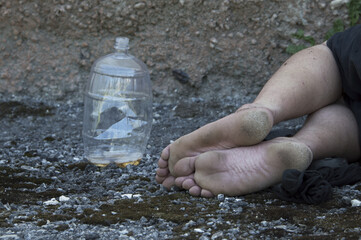 Dirty feet of a drunk homeless man lying on the ground next to an empty bottle. Close up.