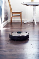 Close up of Robotic vacuum cleaner on laminate wooden floor cleaning in the kitchen. Smart cleaning technology. Selective focus with copy space