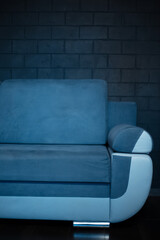 Close-up of part of blue sofa on the background of black brick wall.