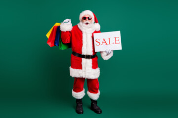 Full length body size view of his he nice fat cheery amazed Santa father carrying gifts presents bargain holding in hand sale promo card season December offer isolated over green color background © deagreez