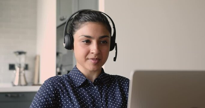 Indian businesswoman wear headset talk with client use laptop videocall app, provide support tell about company services do remote work from home. Applicant pass job interview hiring distantly concept