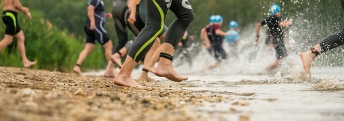Legs of athletes in wetsuits running into a lake at a triathlon competition