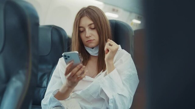 Close up woman travel tourist caucasian at plane removes medical mask use phone smartphone mobile covid-19 respirator girl epidemic virus coronavirus slow motion
