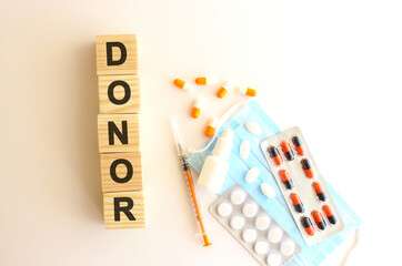 The words DONOR is made of wooden cubes on a white background with medical drugs and medical mask. Medical concept.