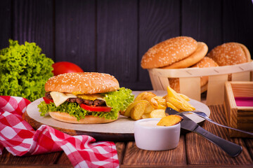 juicy burger on a plate with a red napkin and potatoes on a black wooden background