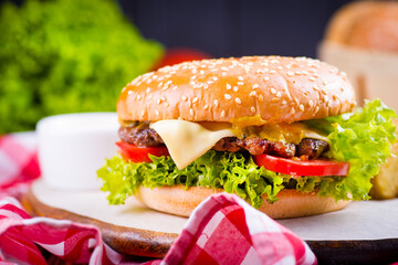juicy burger on a plate with a red napkin and potatoes on a black wooden background