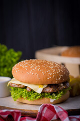 juicy burger on a plate with a red napkin and potatoes on a black wooden background