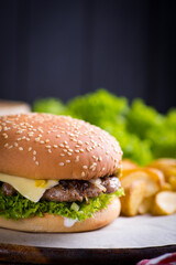 juicy burger on a plate with a red napkin and potatoes on a black wooden background