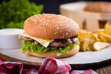 juicy burger on a plate with a red napkin and potatoes on a black wooden background