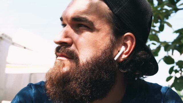 Close up footage of bearded hipster man sitting outdoor and using earpods