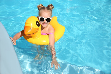 Happy little girl with inflatable ring in outdoor swimming pool on sunny summer day. Space for text