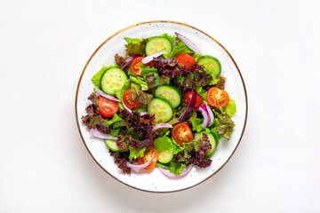 Healthy vegetable salad of red cherry tomatoes, cucumber slices, green and purple lettuce leaves, onions and olive oil in plate on white table Top view Flat lay Diet, mediterranean menu Vegan food