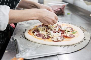 Chef_ÔøΩÔøΩs hands putting toppings on fresh pizza dough
