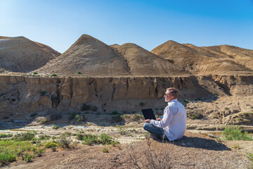 Traveler man working with laptop sitting on rocky mountain on beautiful scenic clif