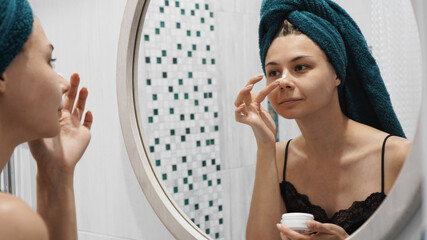 A shot of a young beautiful woman applying lotion to her face