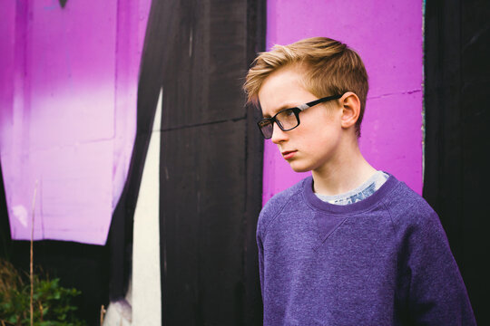 A teenage boy in glasses standing in front of a purple wall