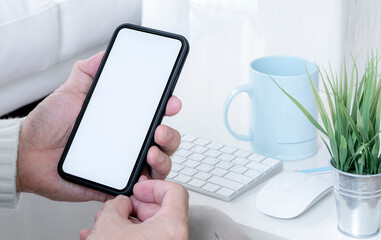 Closeup view of man hand holding blank screen smartphone while sitting in living room at home.