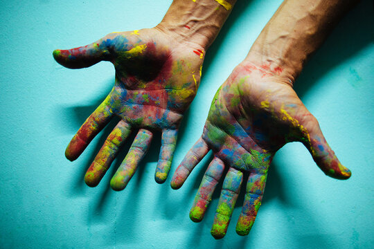 Colourful painted male hands in front of a blue wall