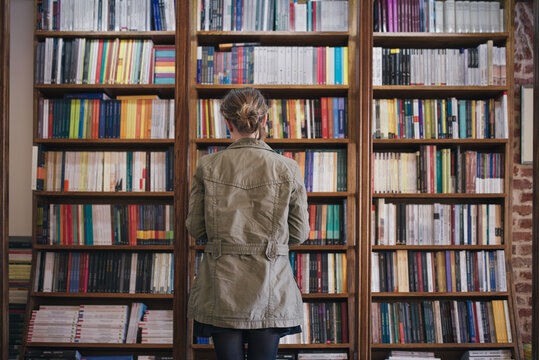 Woman in front of a bookshelf standing with her back towards to camera