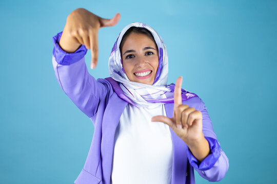 Young beautiful arab woman wearing islamic hijab over isolated blue background smiling making frame with hands and fingers with happy face