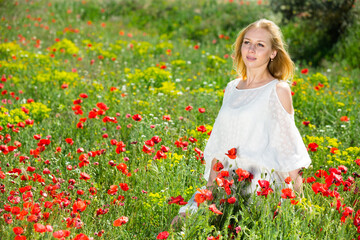 Beautiful woman wearing white dress in poppy field and enjoying summer day