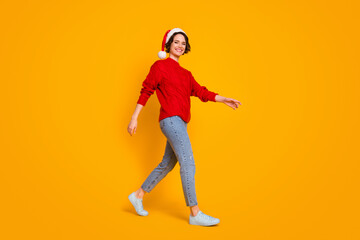 Fototapeta na wymiar Full body profile photo of funny lady good mood walk friends place christmas party festive wear santa cap red knitted sweater jeans footwear isolated yellow color background