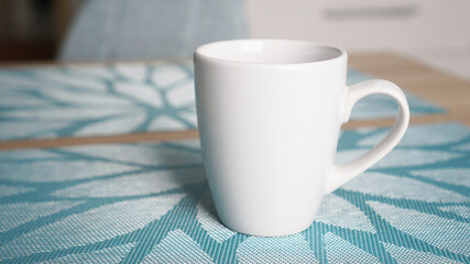 Clean white mug with handle stands on blue table behind blurred kitchen background