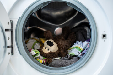 Kleiner brauner Teddybär mit Schmutzwäsche in einer Waschmaschine. Hygiene, Desinfektion,...